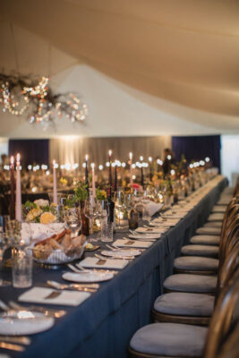 Marquee Furniture set up for wedding with blue table cloths and tall lit candles lining the tables