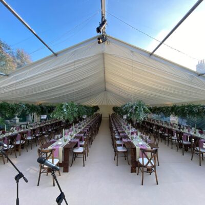 Long lined tables with pink decoration inside marquee with clear roof and microphones set up for autumn wedding